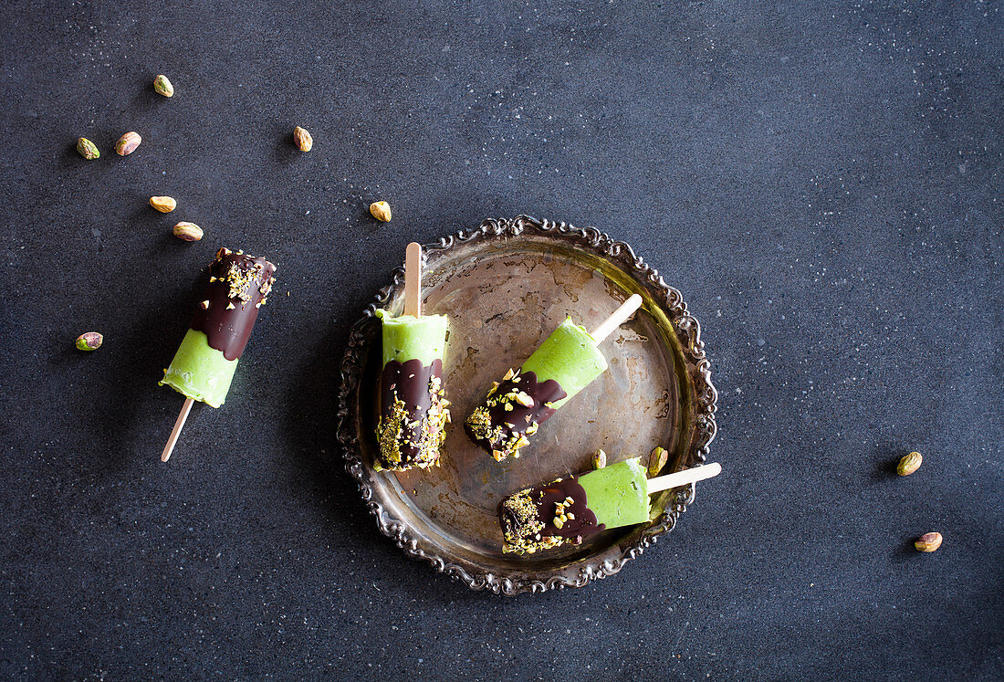 Avocado popsicles covered with dark chocolate and crushed pistachios