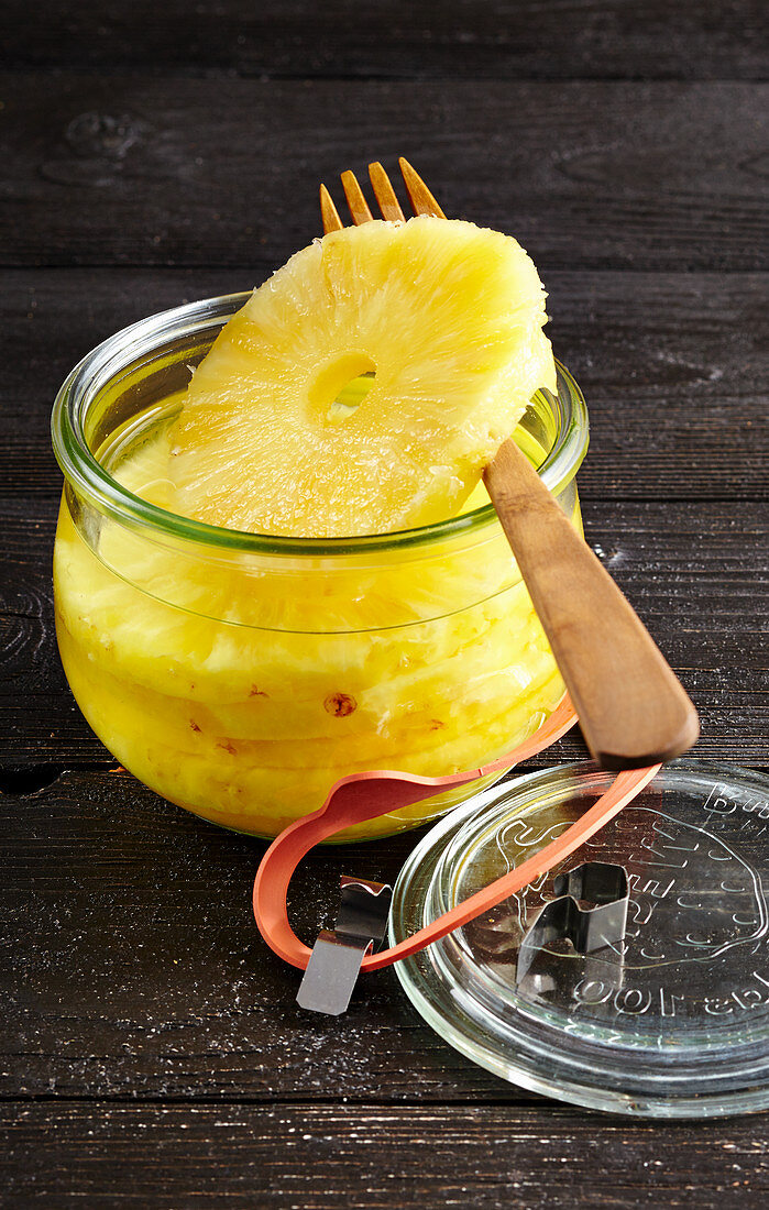 Preserved pineapple slices in a jar with a wooden fork
