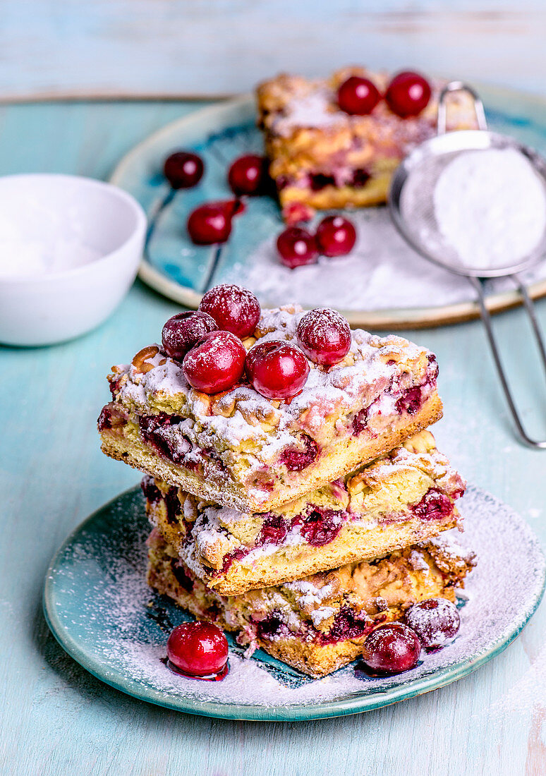 Pieces of cake stacked with frozen cherries, sprinkled with powdered sugar