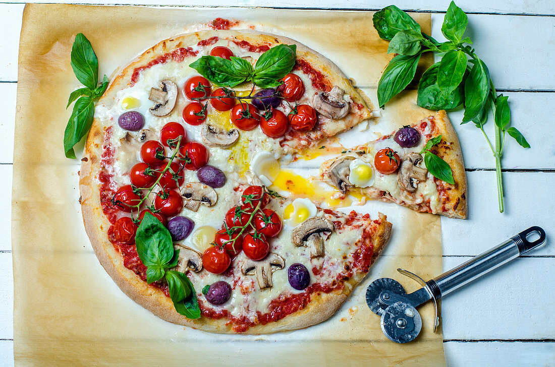 Homemade pizza with mushrooms, olives, quail eggs, cherry tomatoes and fresh basil