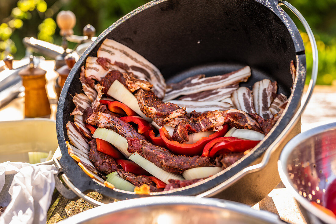 A pot being lined with bacon and layered with meat, onions and peppers
