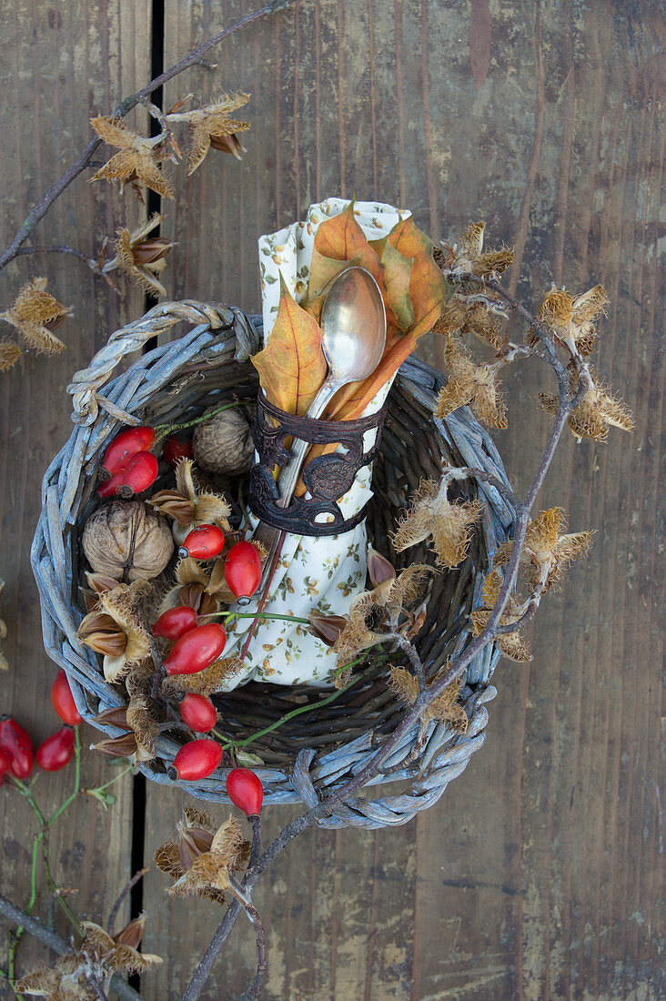 A napkin and cutlery in a basket decorated with rosehips, walnuts and beehnuts