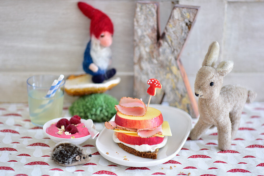 A slice of bread topped with apple, ham and cheese with raspberry cream and lemonade