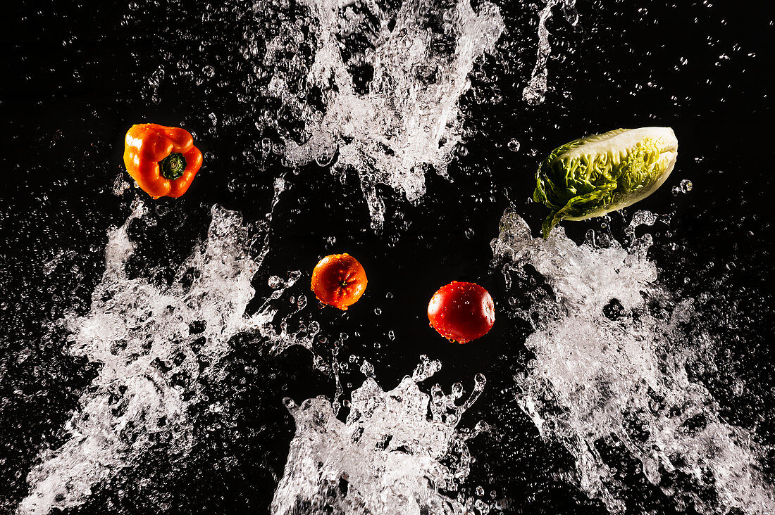 Levitating ripe vegetables and salad in clear splashes of water on black background
