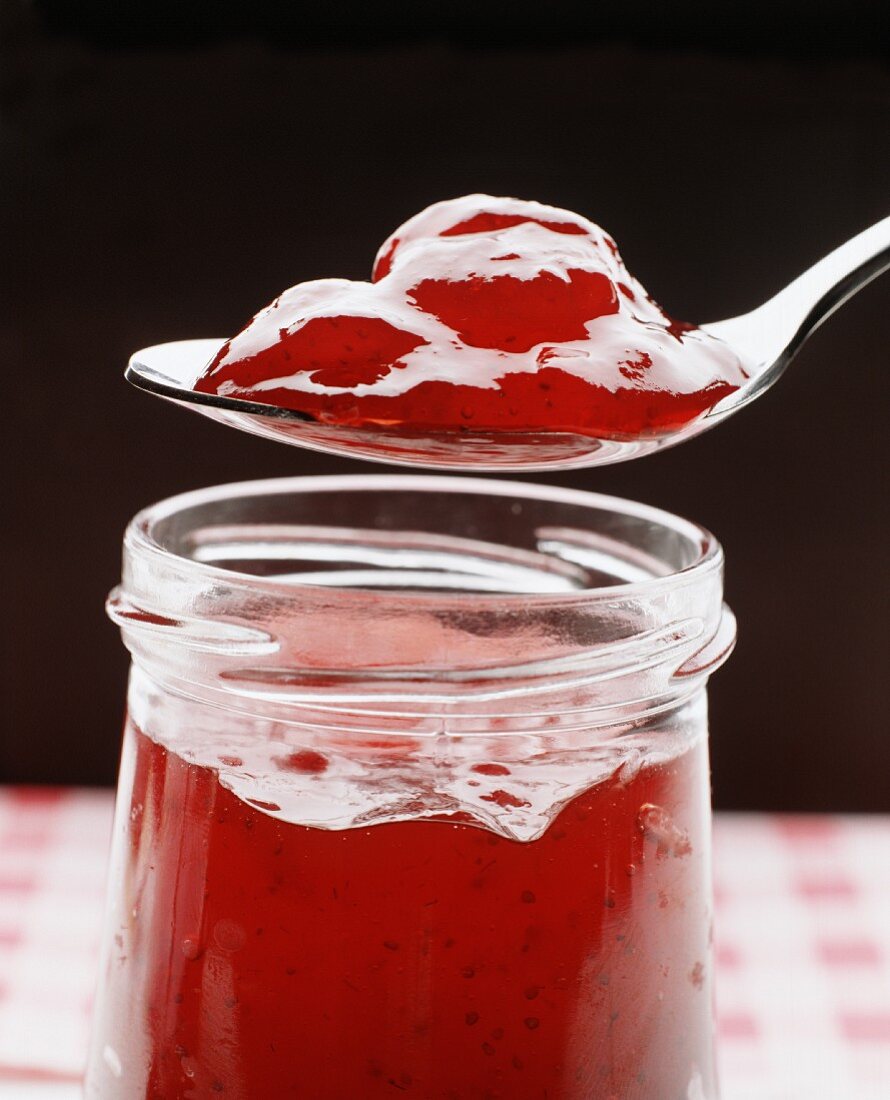 Cold-stirred strawberry jam on spoon above jar