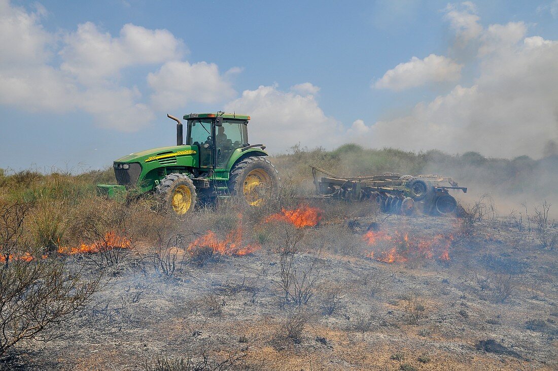 Farmer ploughs a burning field to contain the fire
