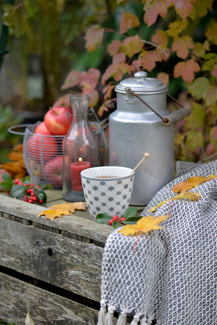 Old wine crate decorated for autumn with apples, milk churn and cup of tea