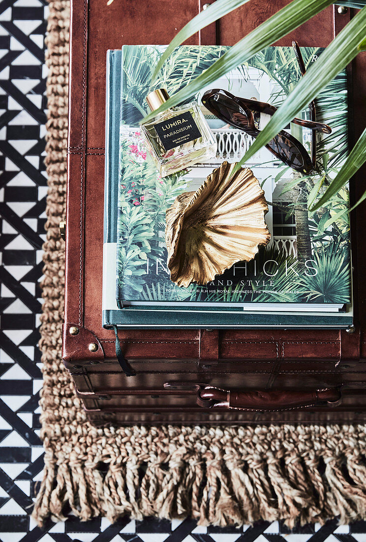 Brown suitcase as a storage table on top of books, perfume and sunglasses