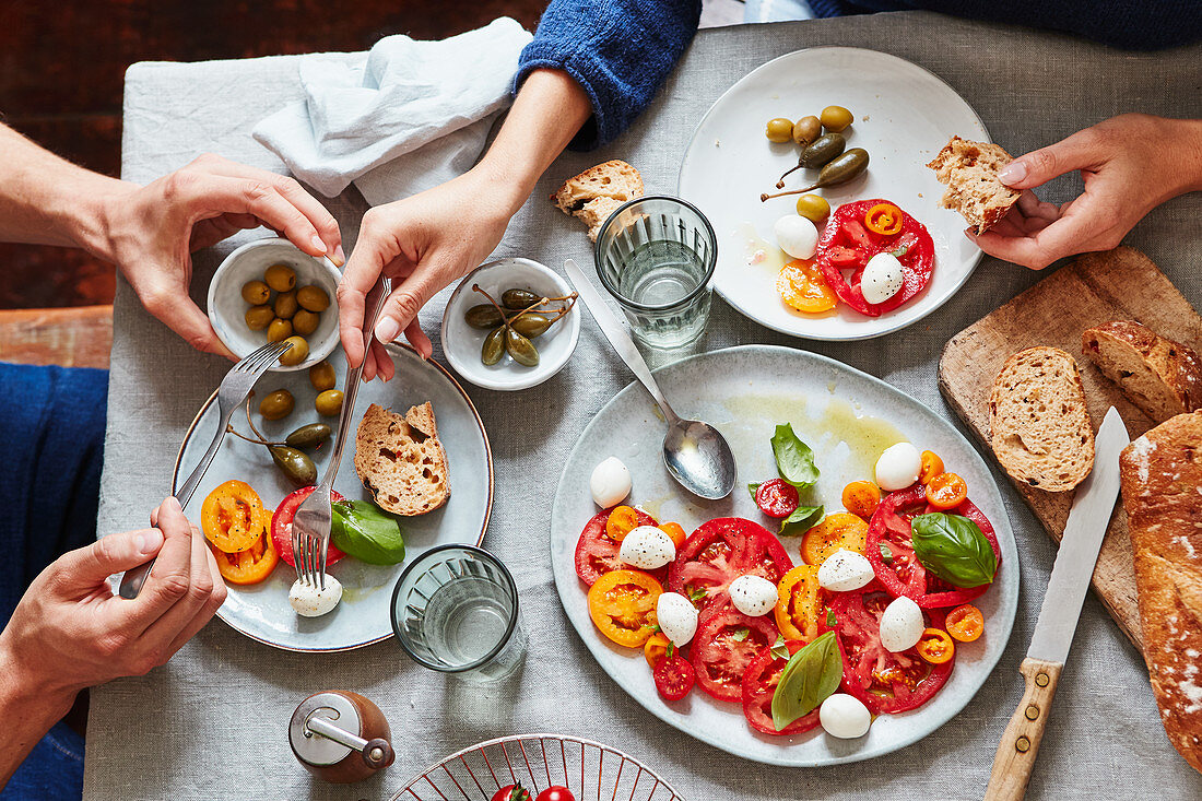 A couple eating tomatoes with mozzarella, olives and capers