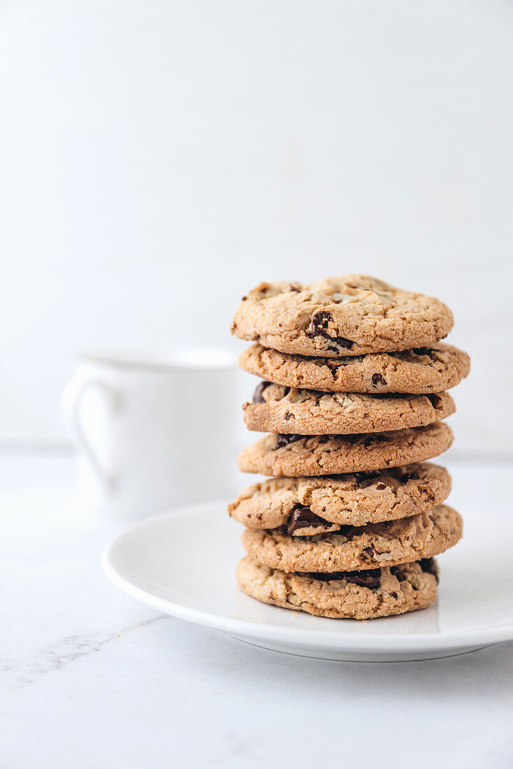 A stack of chocolate chip cookies with a cup of milk in the background