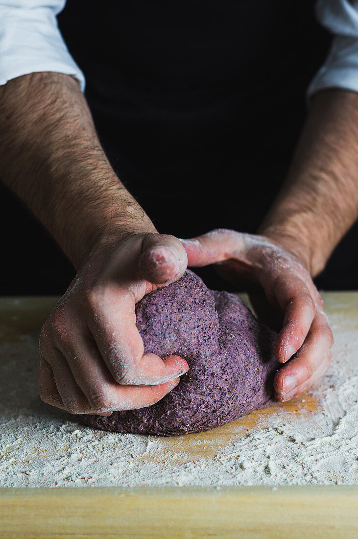 A man kneading a purple bread dough on a floured wooden surface