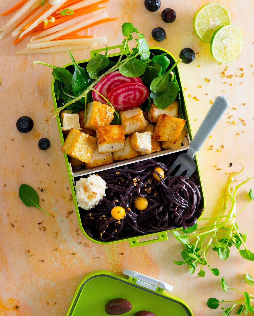 A bento box with tofu, black pasta, celery purée, spinach salad and beetroot