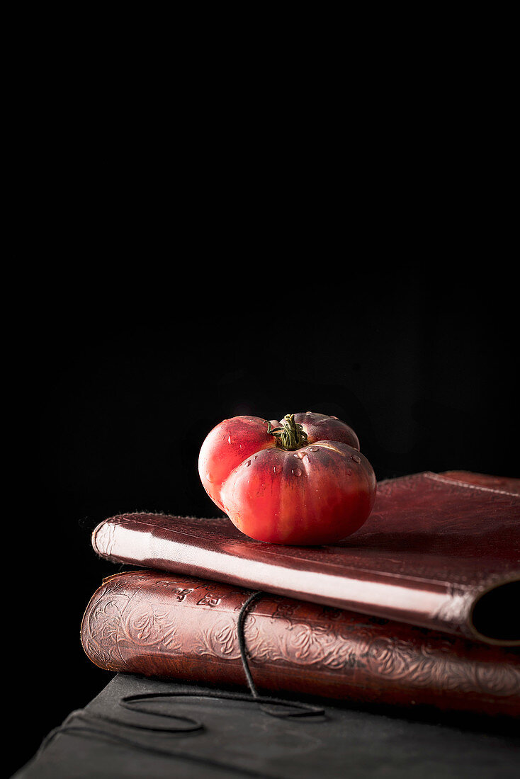 Ripe red tomato placed on stack of ancient books against black background