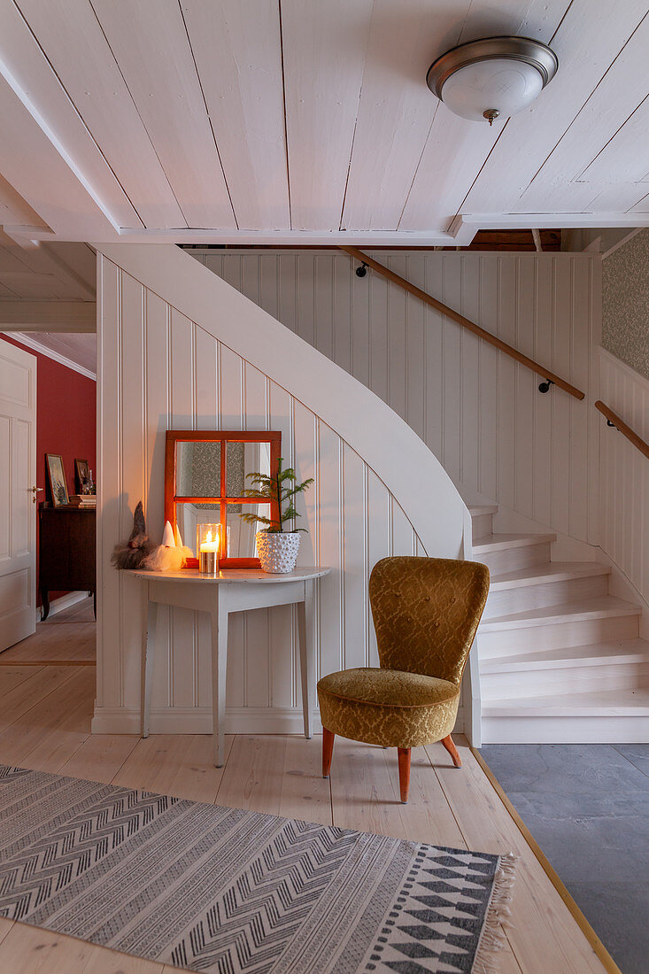 Easy chair and console table at foot of staircase in foyer