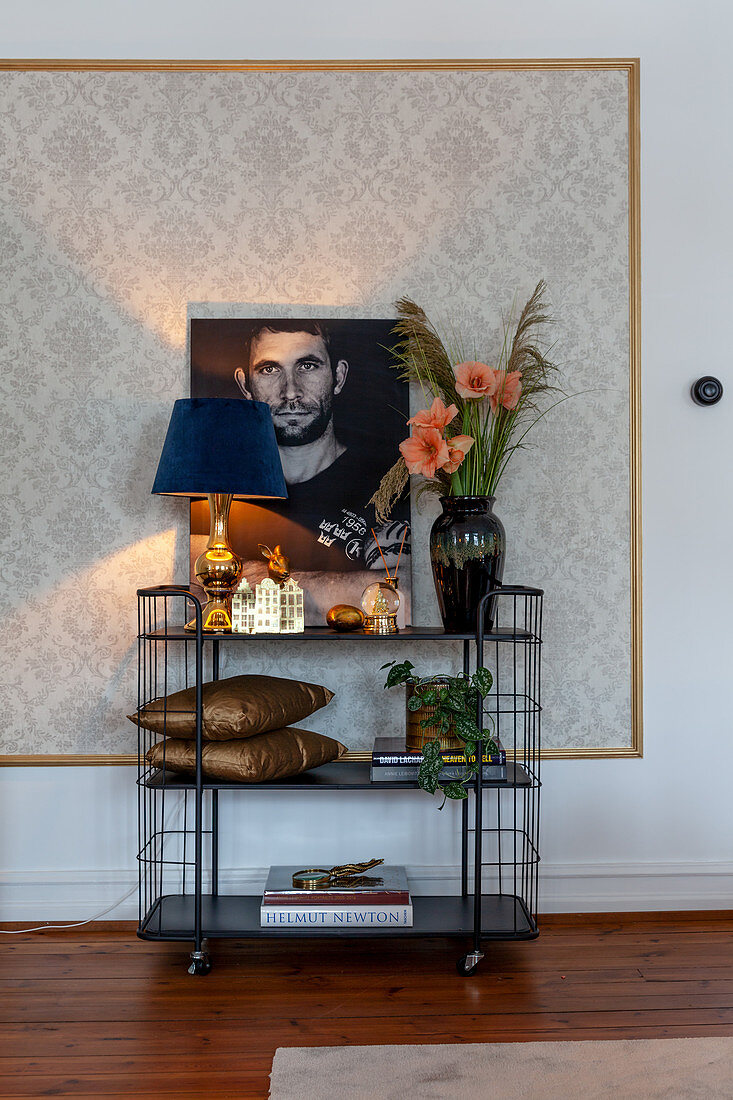 Elegantly decorated serving trolley against wall with panel of patterned wallpaper