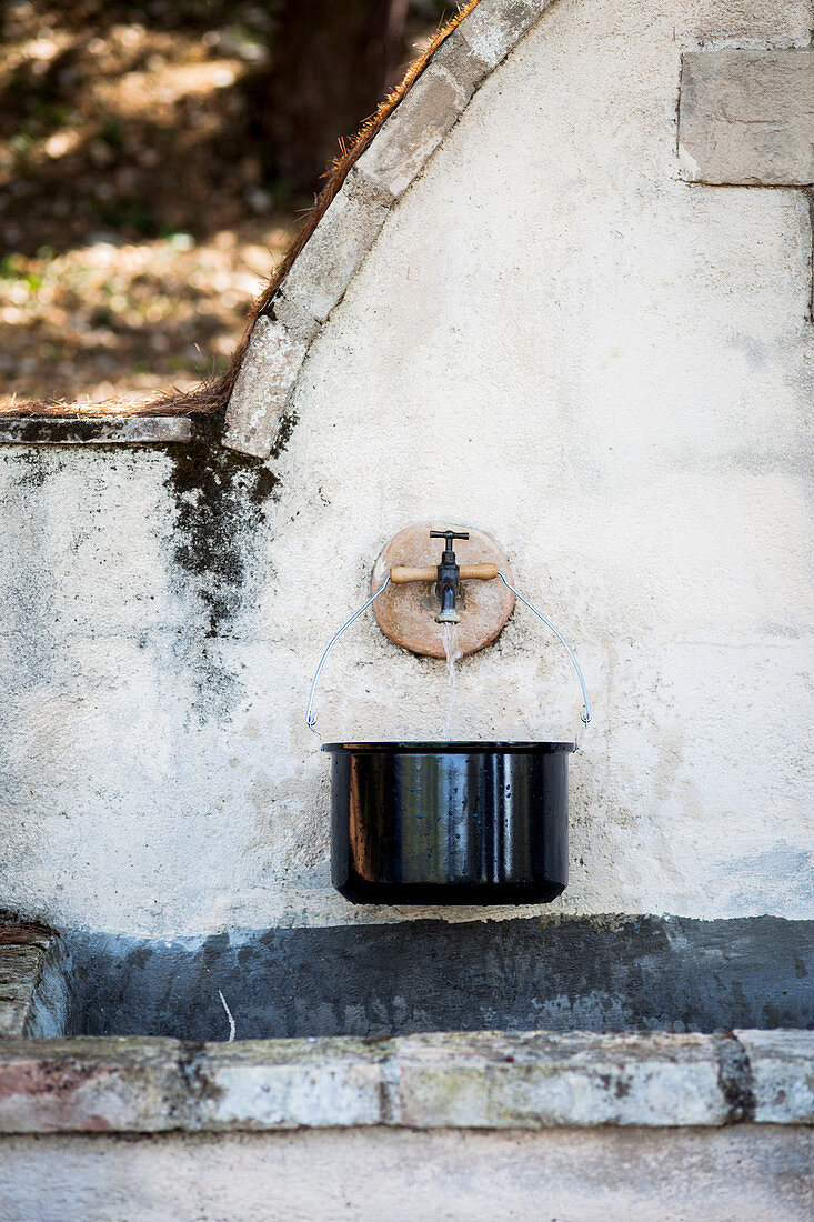 Saucepan below tap of stone fountain