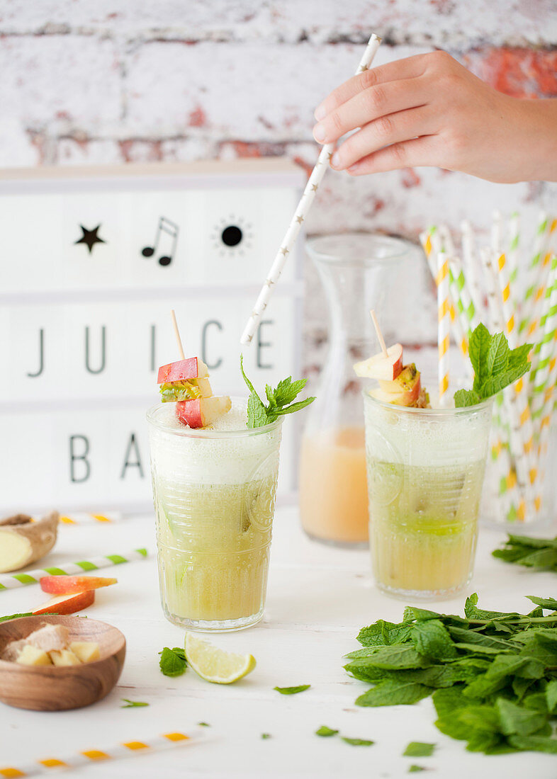 Adding a straw to a glass of pineapple fruit juice with mint, ginger and lime