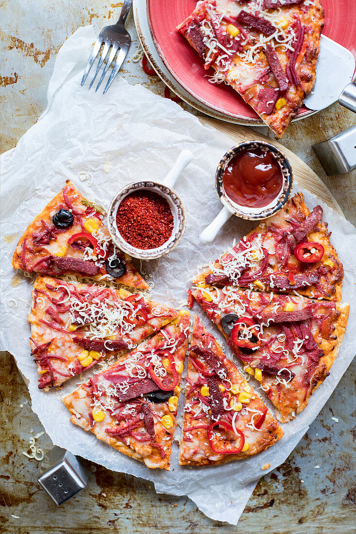 Pikante Pizza mit Würstchen, Mais und Oliven