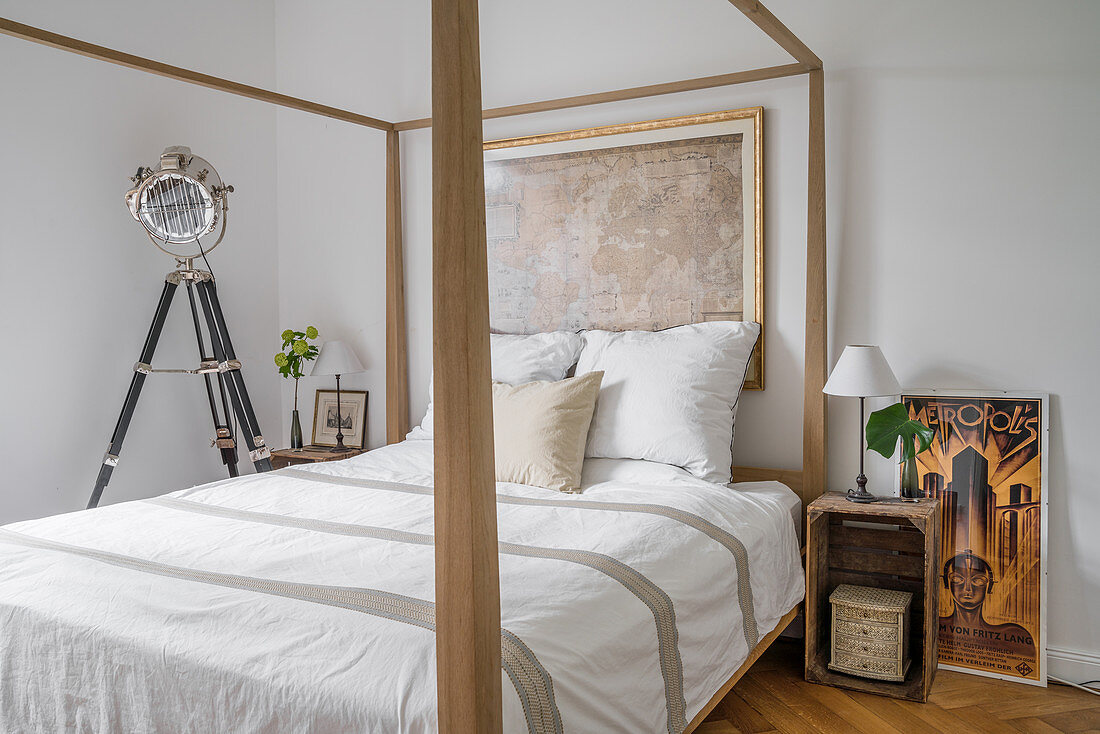 Pale, wooden four-poster bed, studio lamp and wooden crate used as bedside table