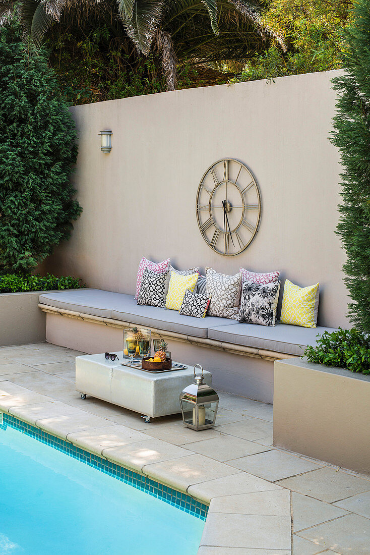 Sichtschutzwand mit integrierter Sitzbank und Wanduhr am Pool im Garten