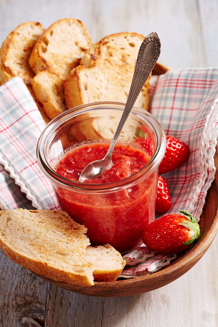 Homemade strawberry chutney in a preserving jar with bread, a napkin and a wooden bowl