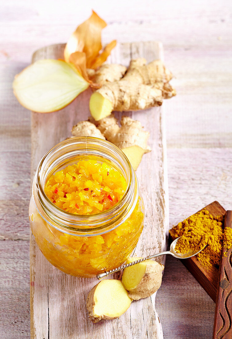 Pineapple and onion chutney with curry and fresh ginger in a jar on a wooden surface