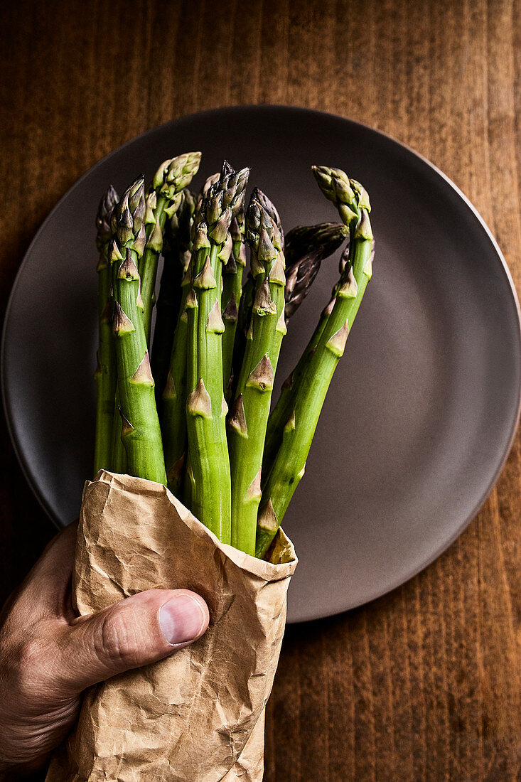Hand holding a bundle of fresh green asparagus in a paper bag