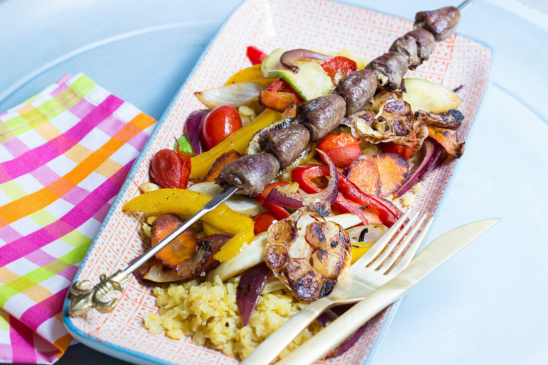 Chicken heart skewer on colourful roast vegetables with yellow lentils