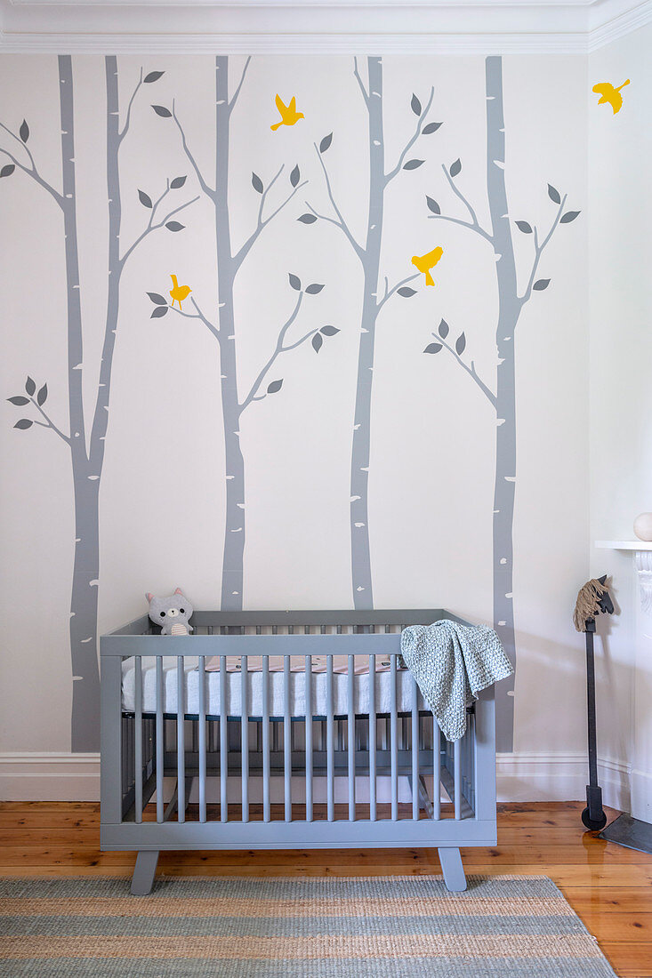 Blaues Gitterbettchen in Babyzimmer mit fröhlicher Wandmalerei