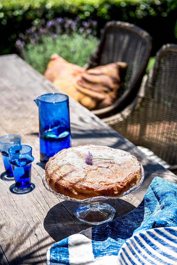 Kuchen auf Kuchenständer daneben blaue Karaffe mit Gläsern auf Terrassentisch