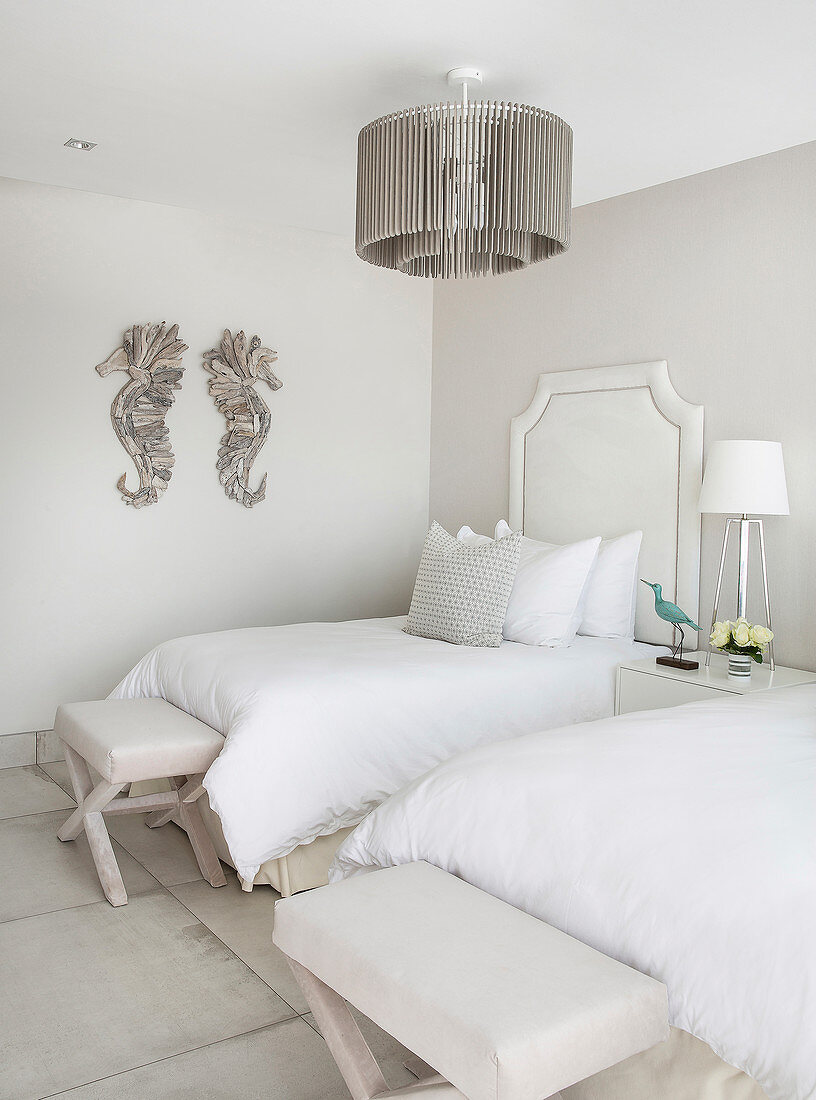 Twin beds with stools at foot ends in beige and white bedroom