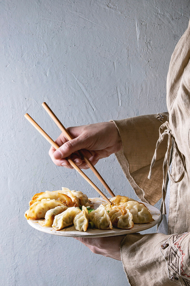 Fried asian dumplings Gyozas potstickers on white ceramic tray and wooden chopsticks in female hands