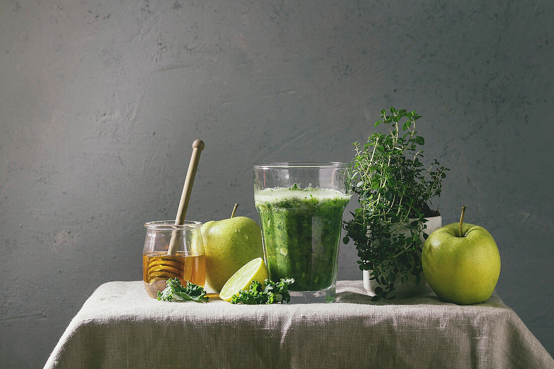 Grüner Smoothie mit Spinat, Kohl und Apfel im Glas umgeben von Zutaten