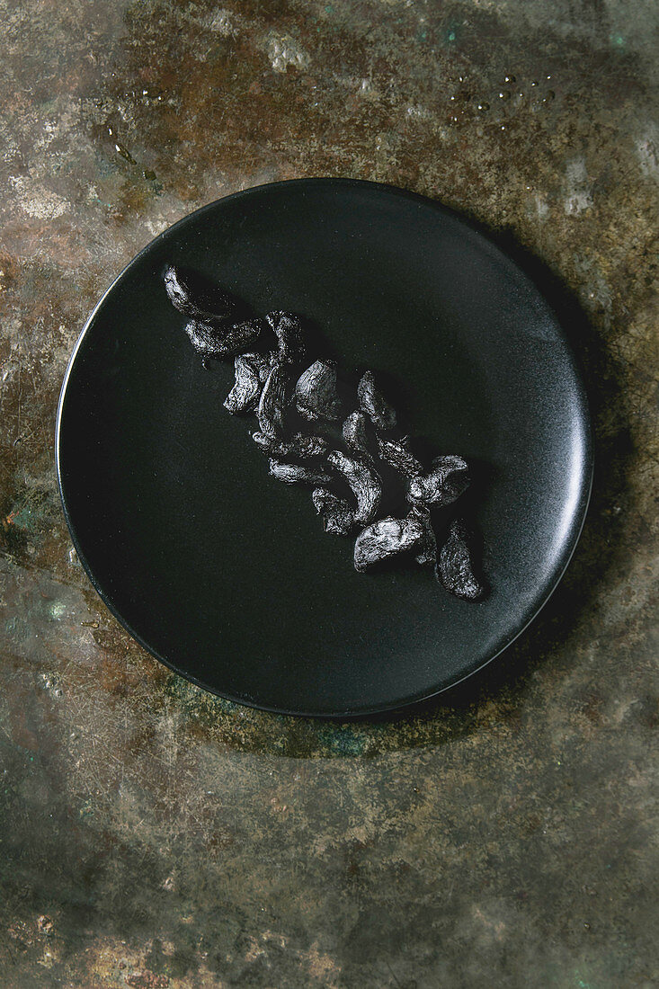 Fermentierte schwarze Knoblauchzehen auf schwarzem Teller