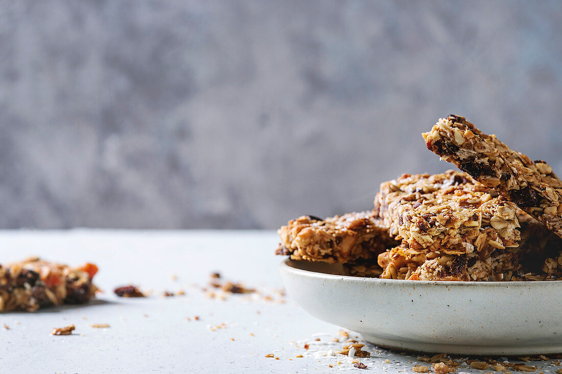 Homemade energy oats granola bars with dried fruits and nuts whole and broken in ceramic plate on grey table