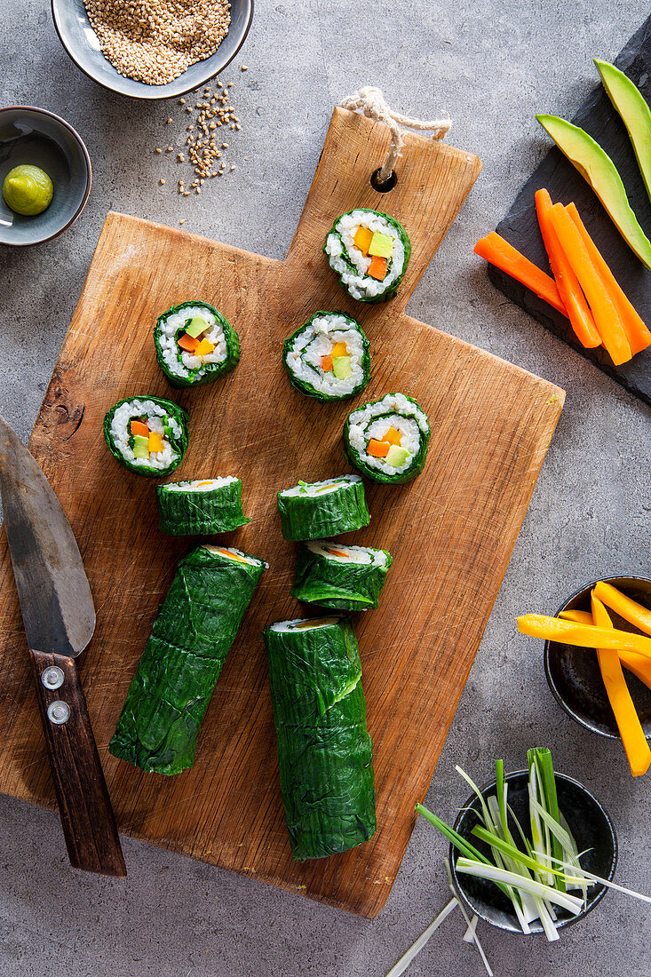 Springlike vegan maki sushi with spinach, avocado, carrots, mango and shallots on wooden board