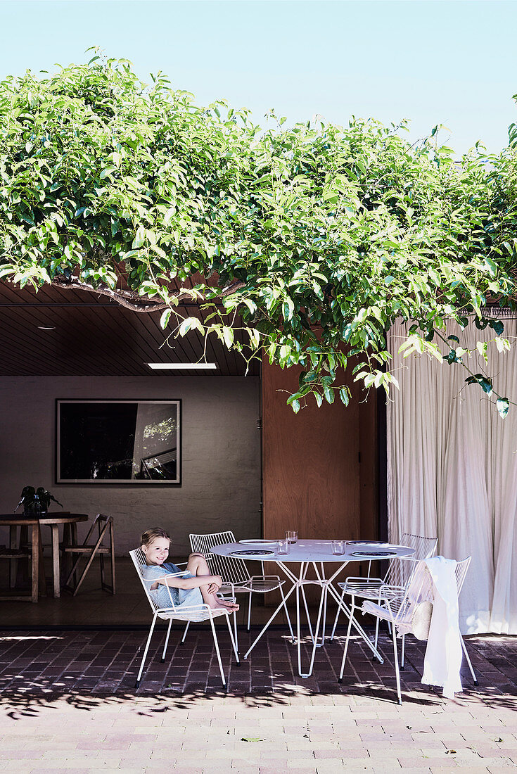 Child sits on the garden chair at the round table on the terrace