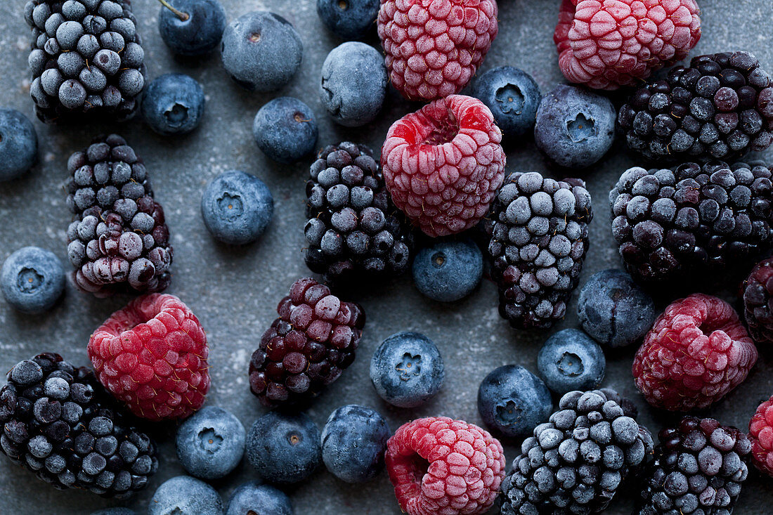 Frozen raspberries, blackberries and blueberries, photographed from above on a blue surface