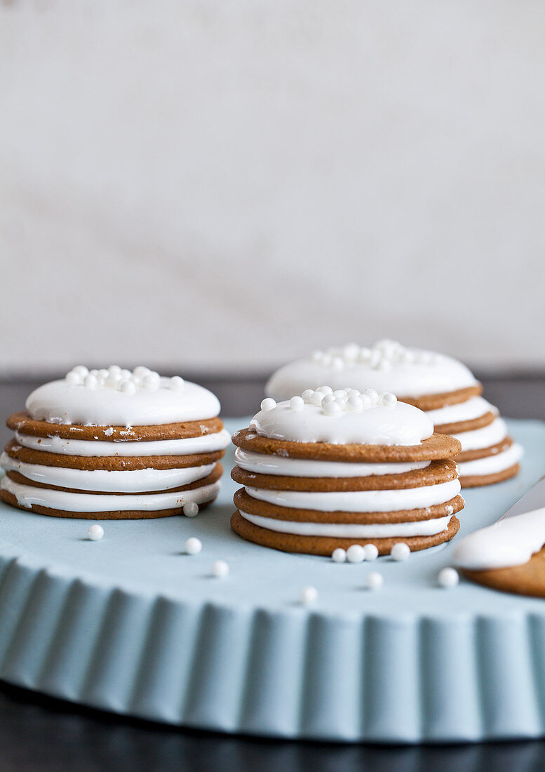 Ginger cookies, topped with marshmallow cream, and white candies, stacked on a blue tray