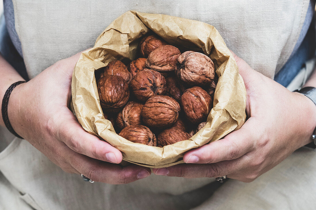 Person holding brown paper bag with fresh walnuts