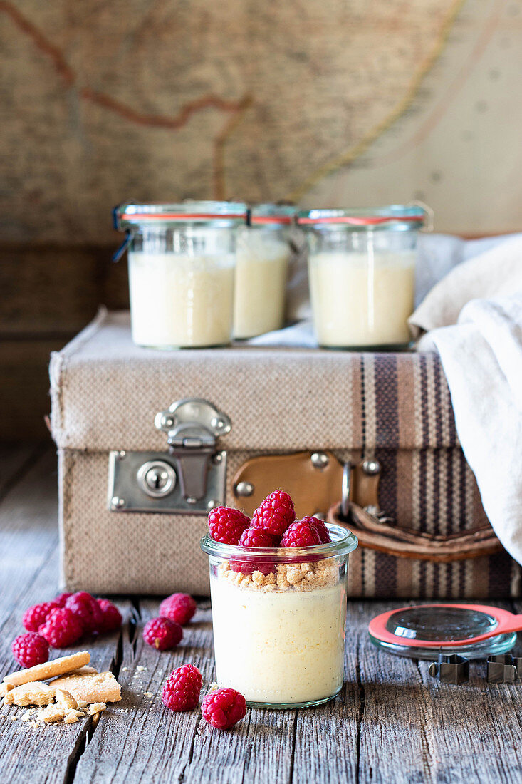 Composition of old suitcase and glass tubs with cheesecake and raspberry placed on wooden table