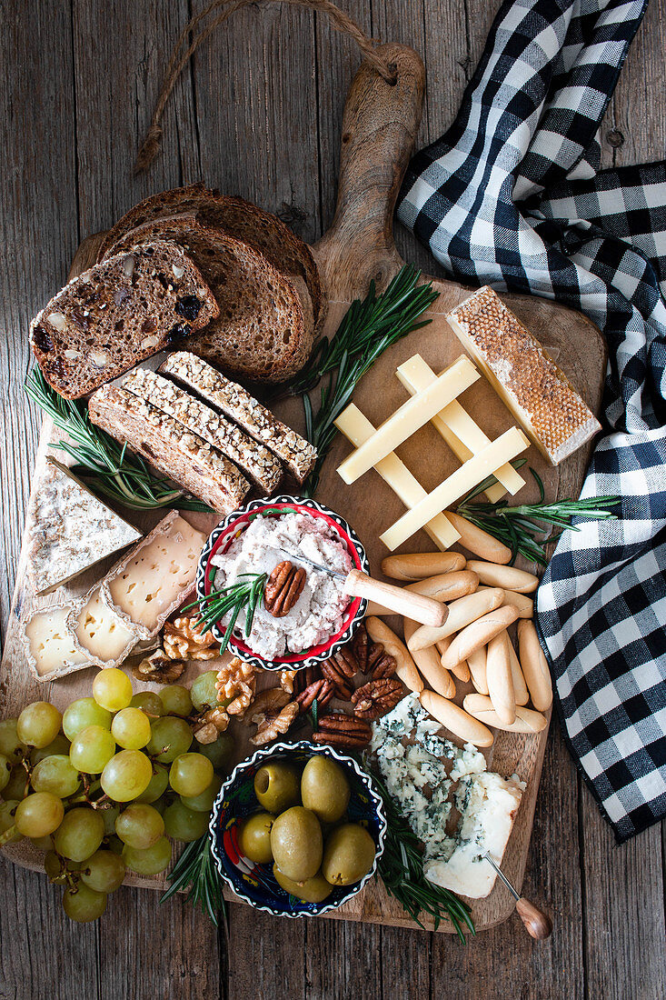 Composition of fresh rye bread, cheese, grape bunch and olives placed on wooden board