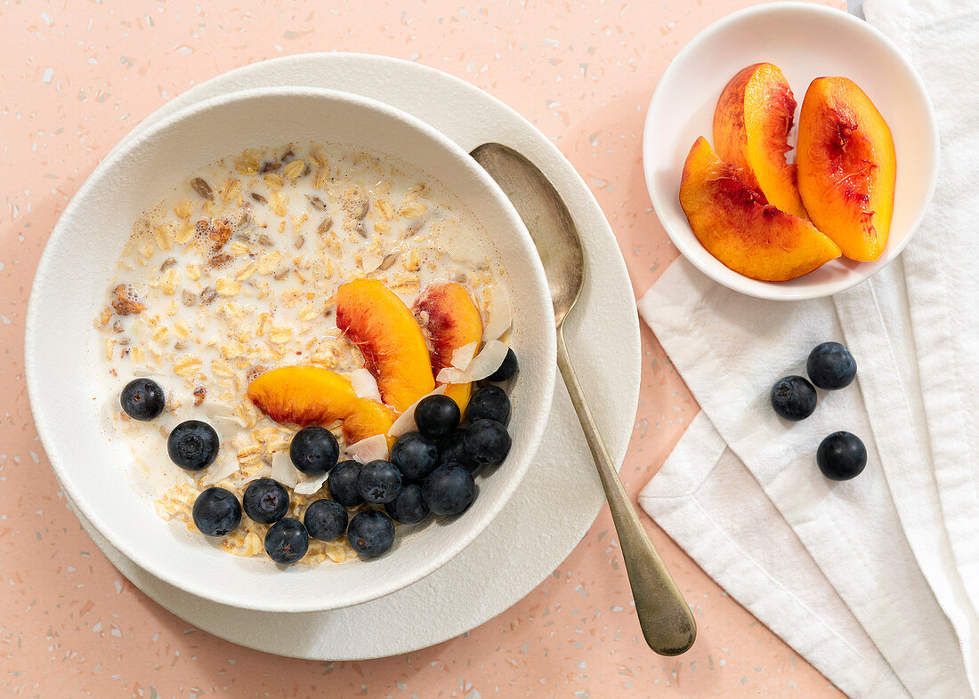 Oats, peach slices, blueberries and milk in a bowl for breakfast