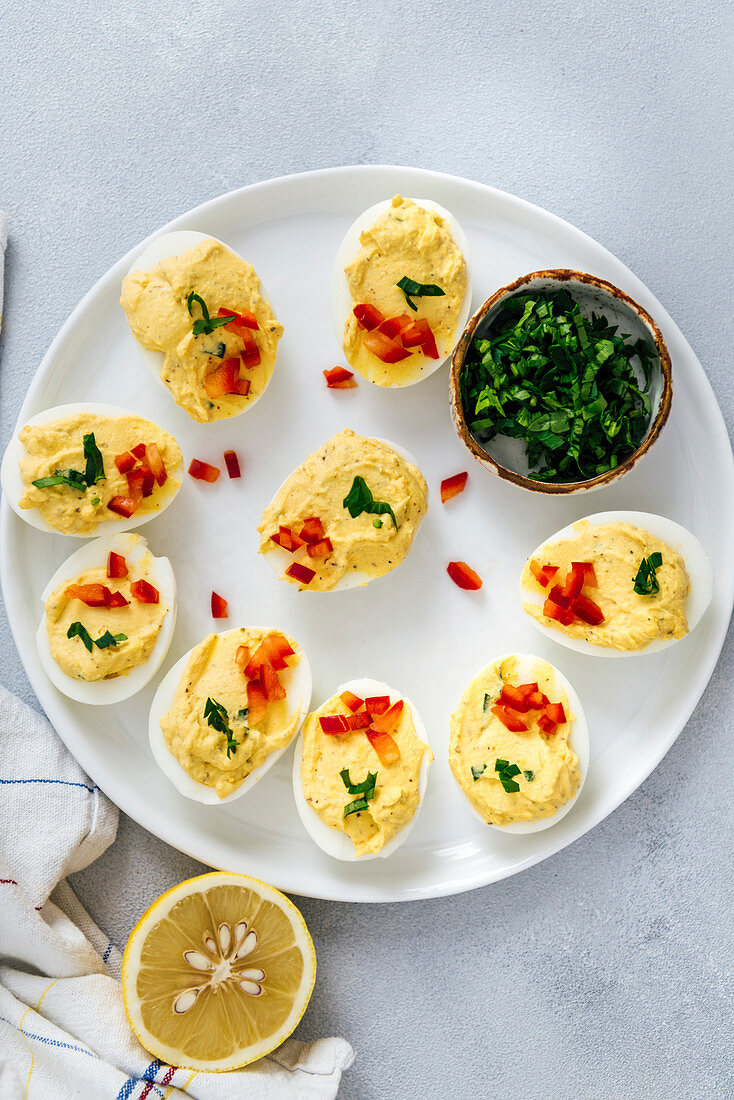 Deviled eggs without mayo garnished with red bell pepper and parsely on a white plate