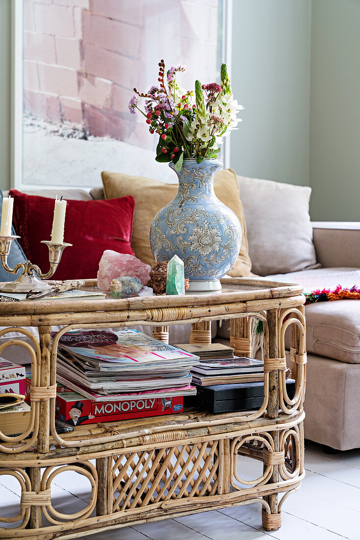 Magazines, games and vase of flowers on vintage-style rattan table in front of sofa