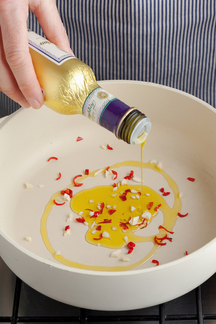 Olivenöl auf gehacktem Knoblauch und Chilischote gießen