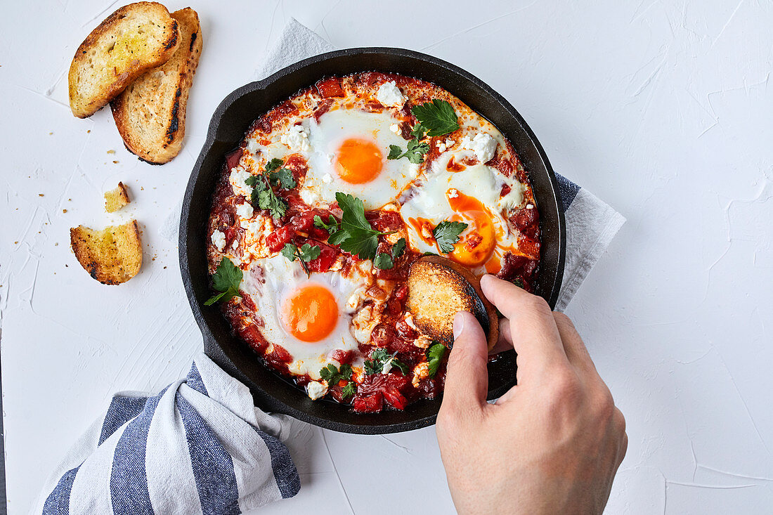 Shakshuka with tomatoes, peppers, onions and eggs prepared in cast iron skillet