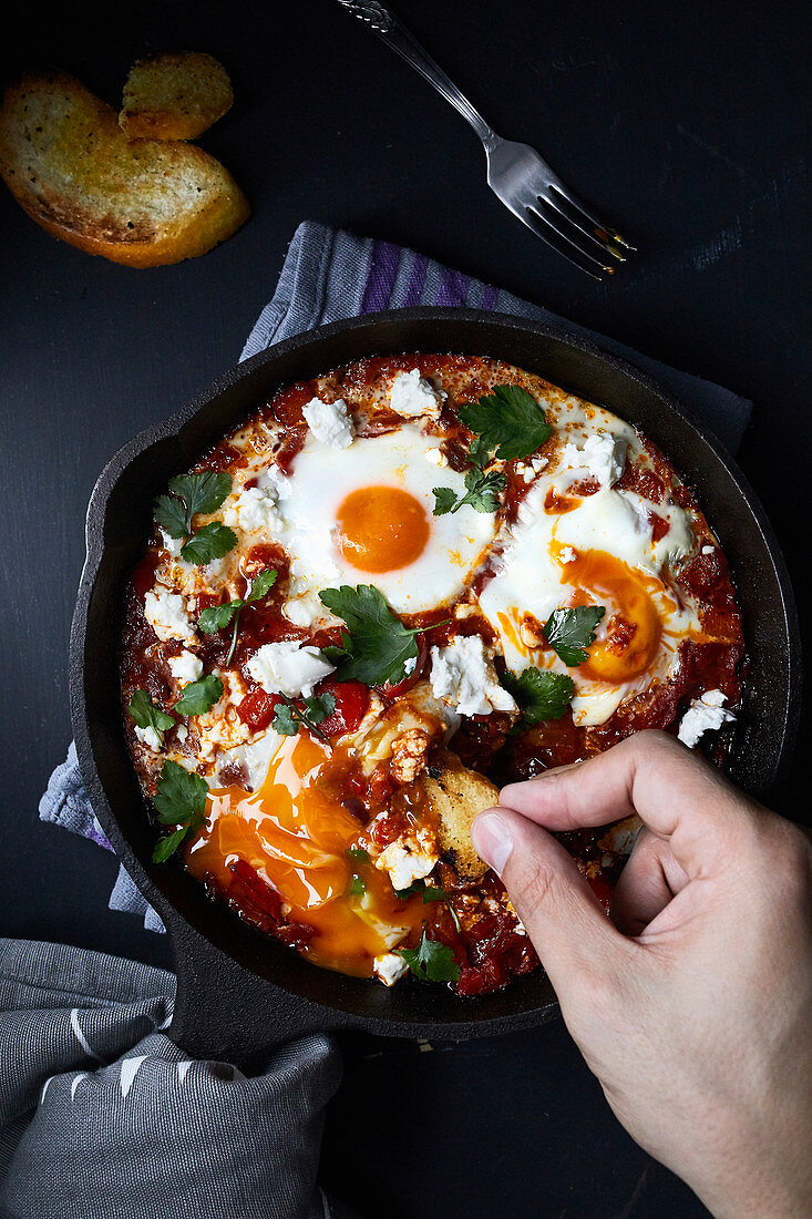 Shakshuka with tomatoes, peppers, onions and eggs prepared in cast iron skillet