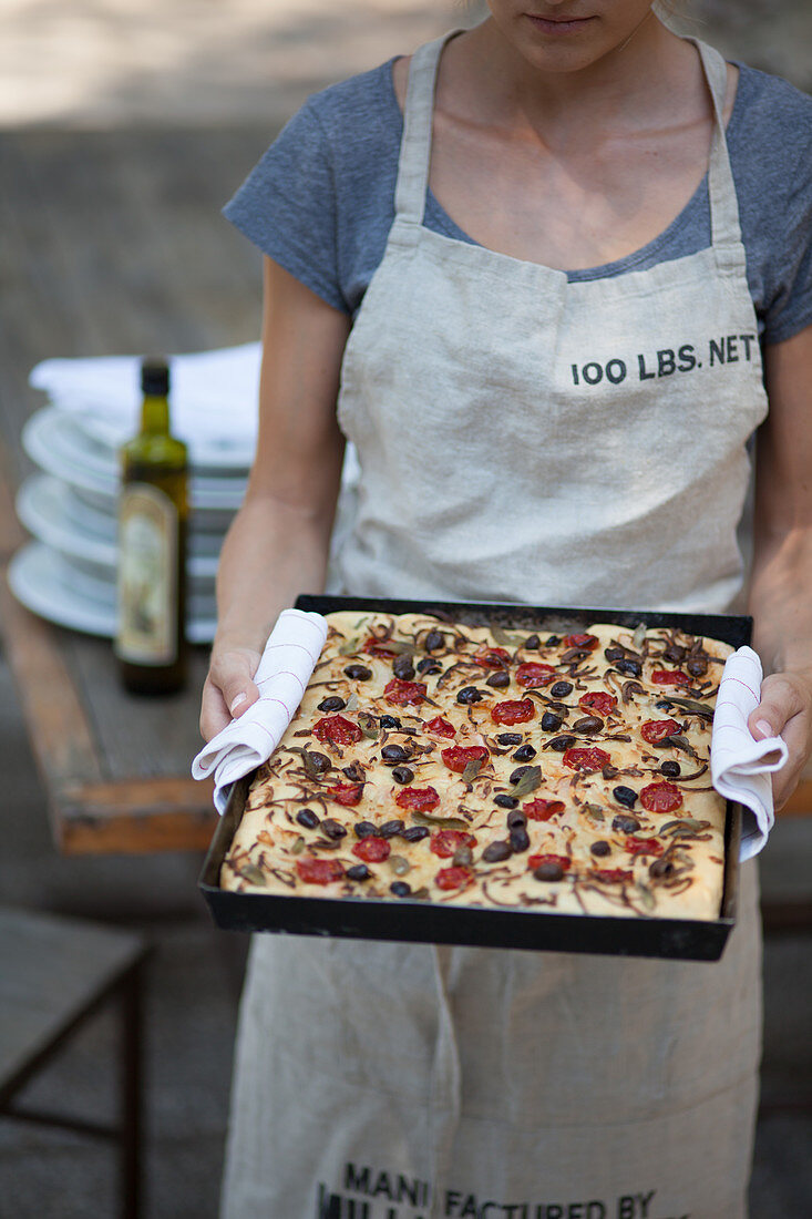A woman holding a baking tray with freshly baked focaccia