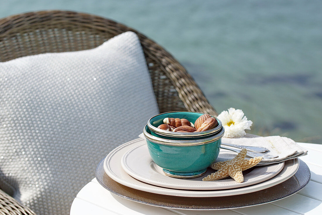 A bowl of chocolates at a place setting with a starfish on a table on the beach